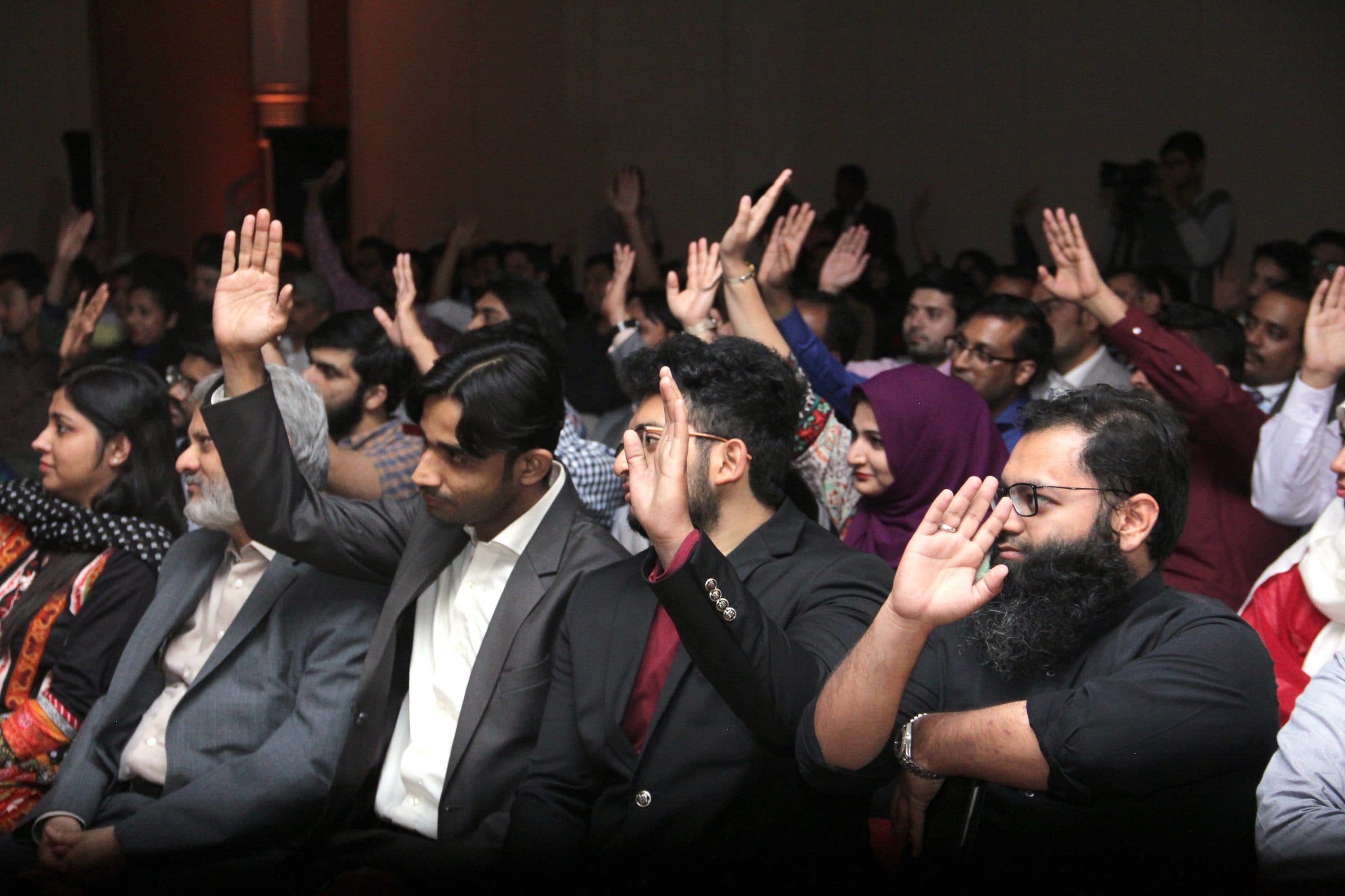 A packed Torque room with dozens of participants' hands in the air, mid-session