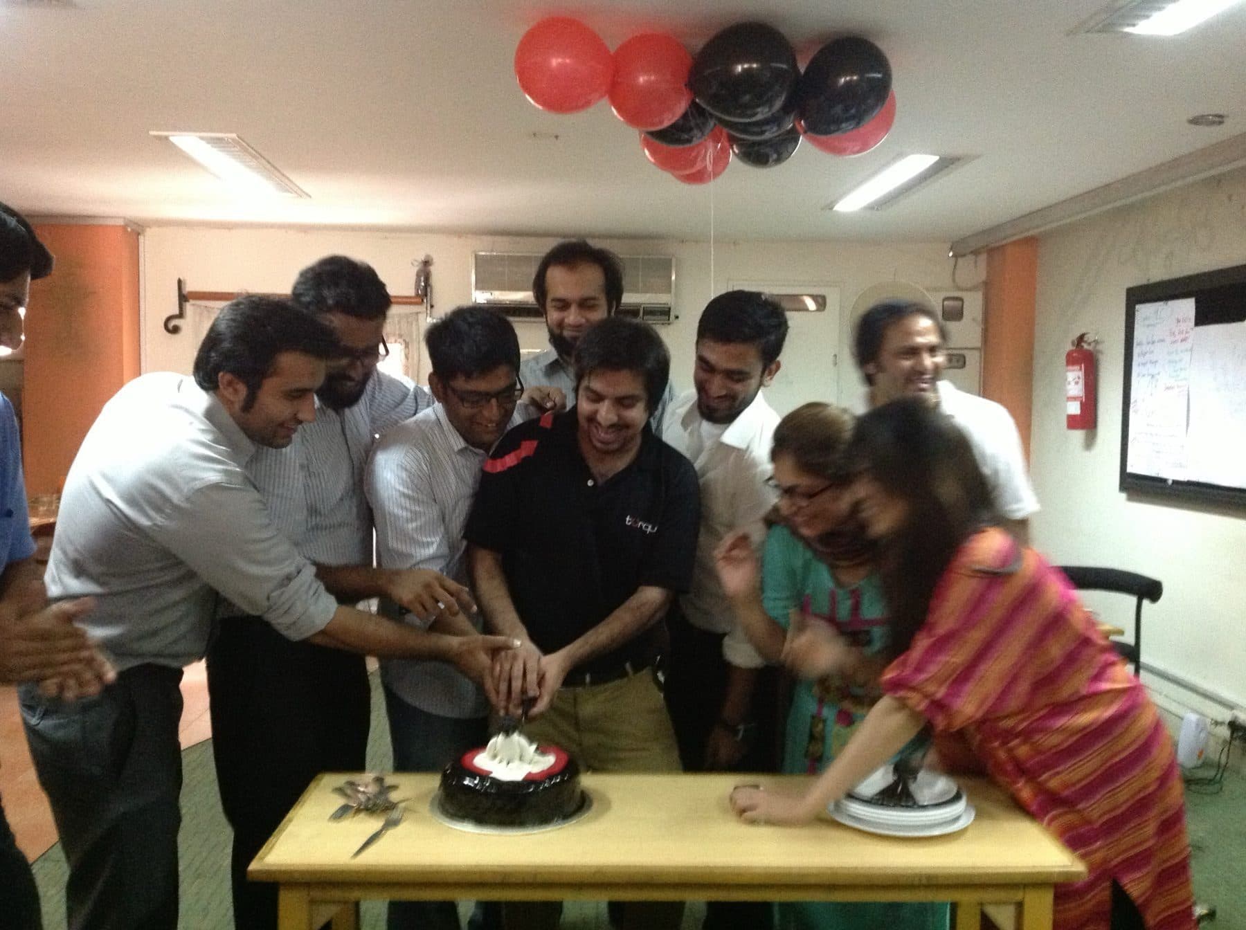 The Torque team crowded around a cake in the office, under black and red balloons