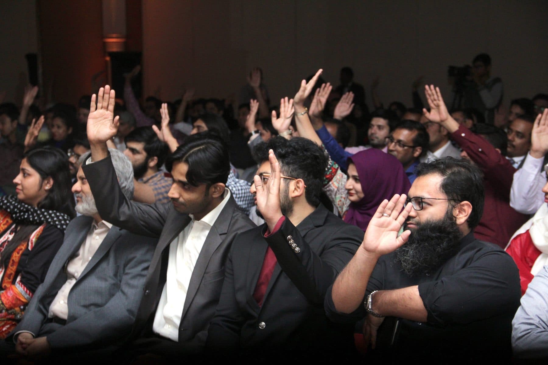 A packed conference room with hands going up across every row