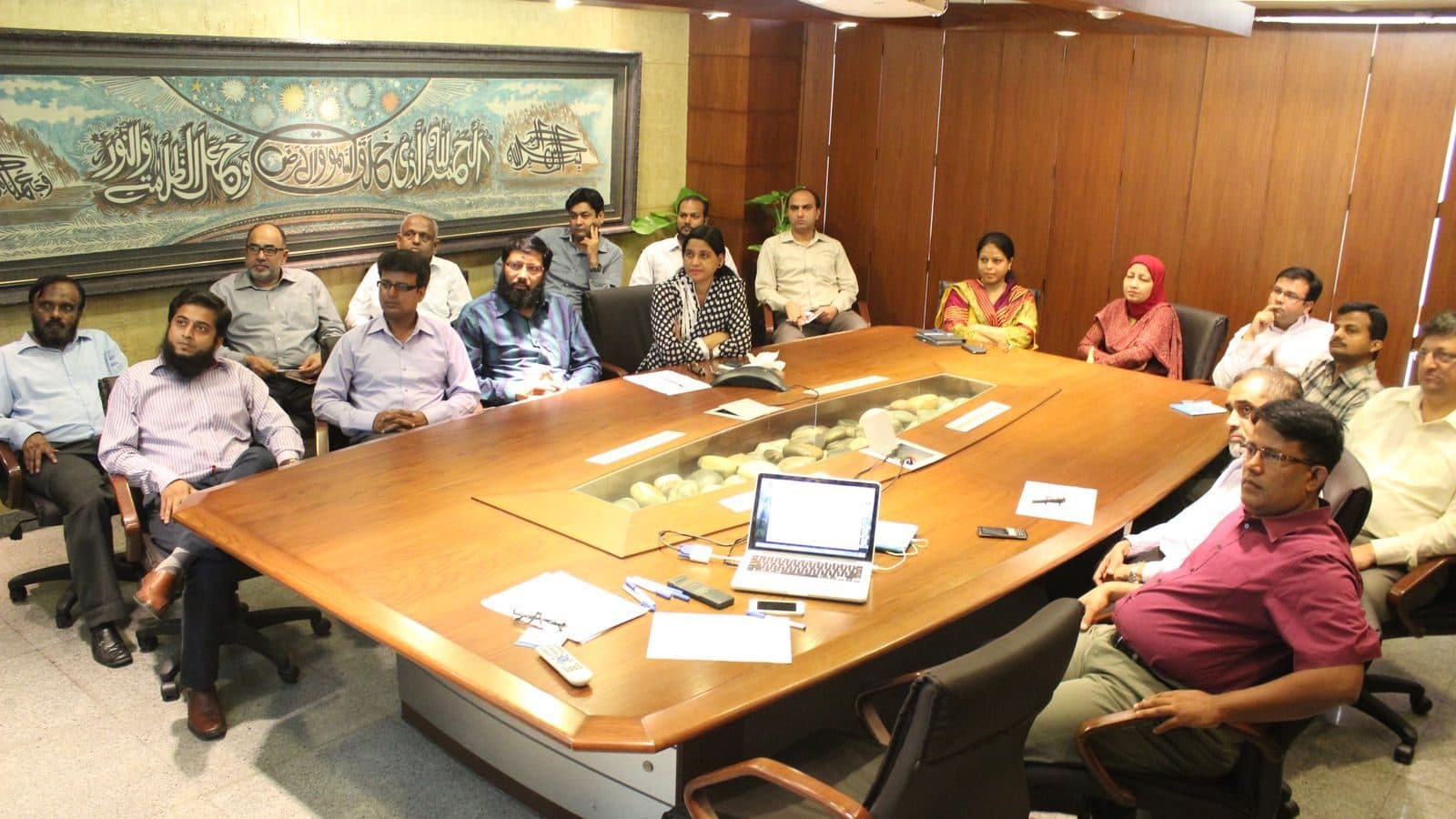 Participants seated all the way round a long boardroom table, laptops and papers open in front of them