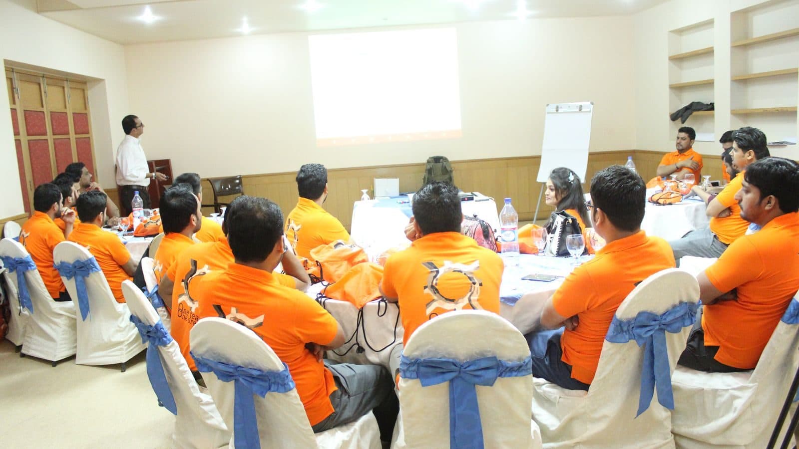 A group in matching orange shirts gathered round tables, turned towards the front of the room
