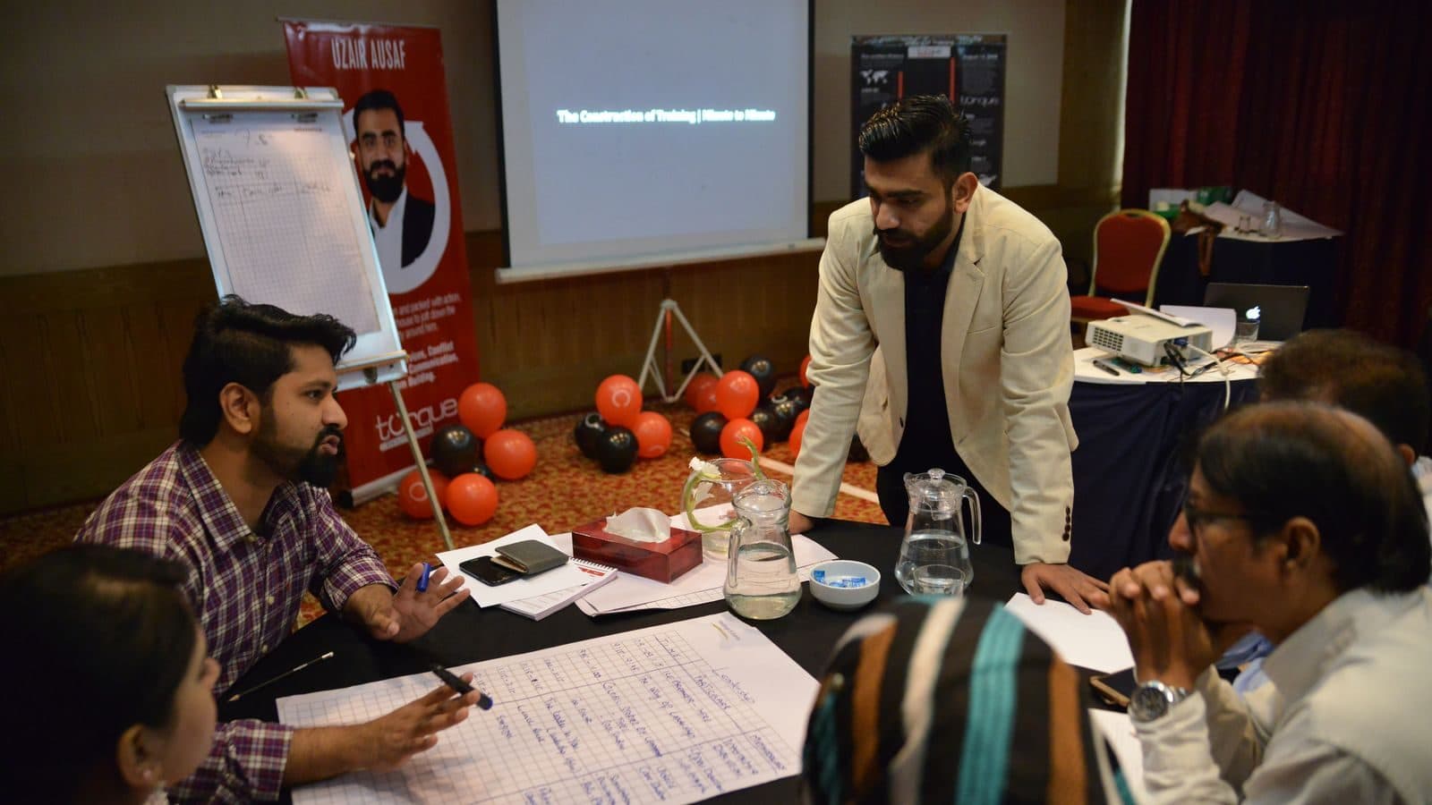 A table of participants taking notes while somebody works a flipchart behind them
